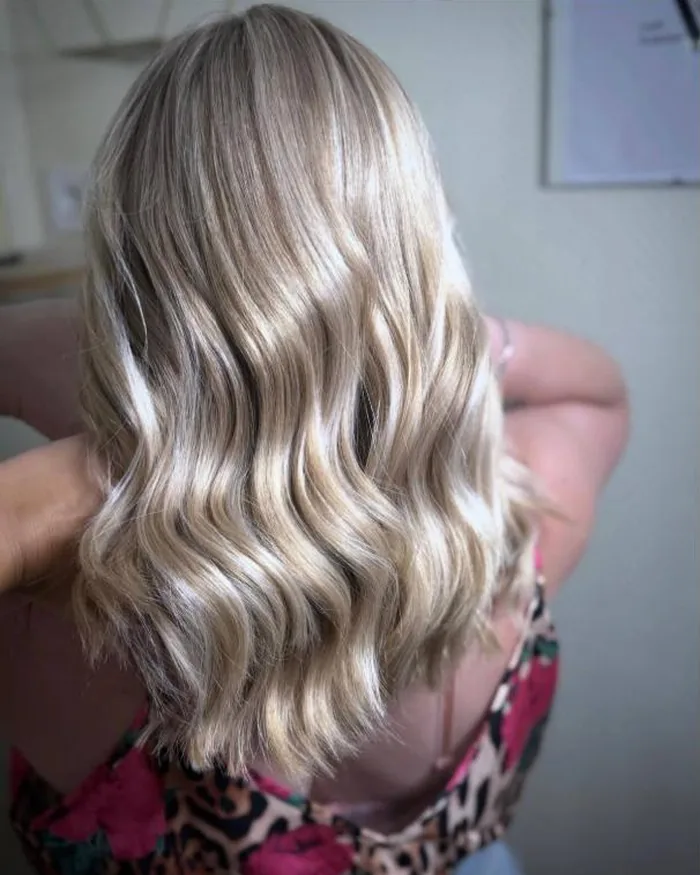 Balayage blond platine bouclé réalisé chez Coiff Evolution, salon de coiffure à Saint-Pol-sur-Mer
